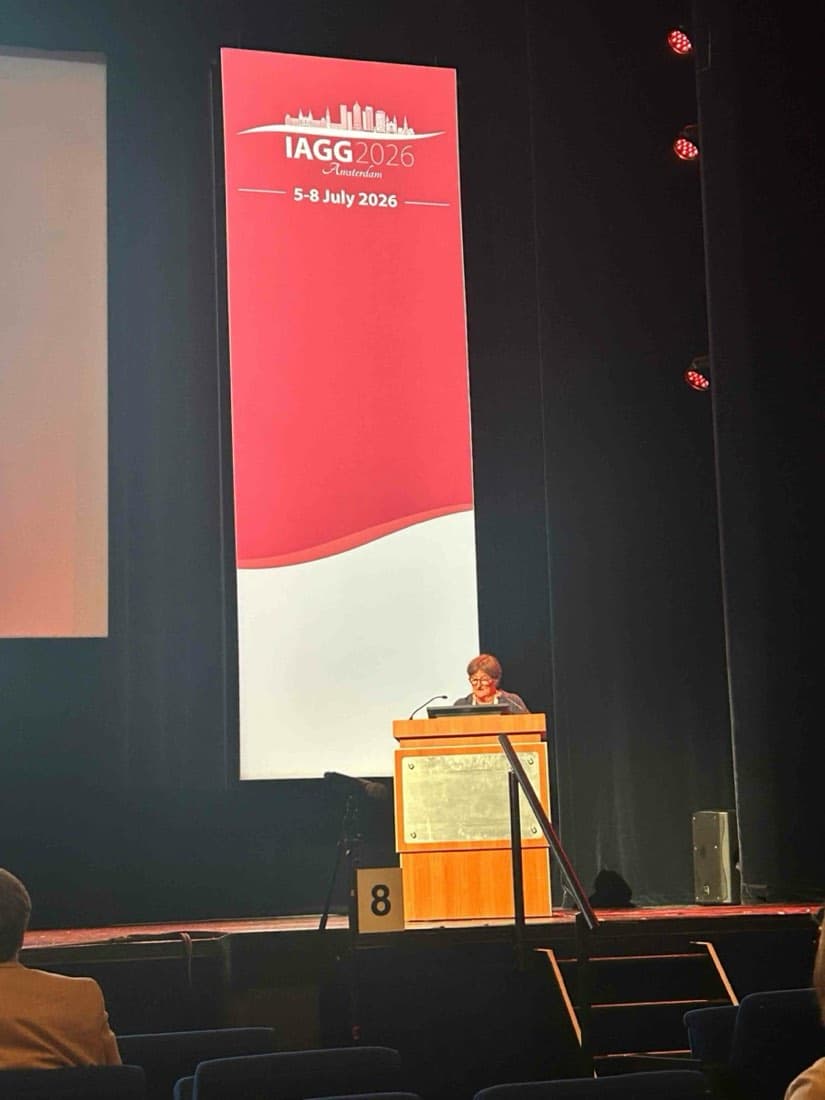 Marja Aartsen står ved talerstolen foran et stort IAGG 2026-banner i konferansesalen